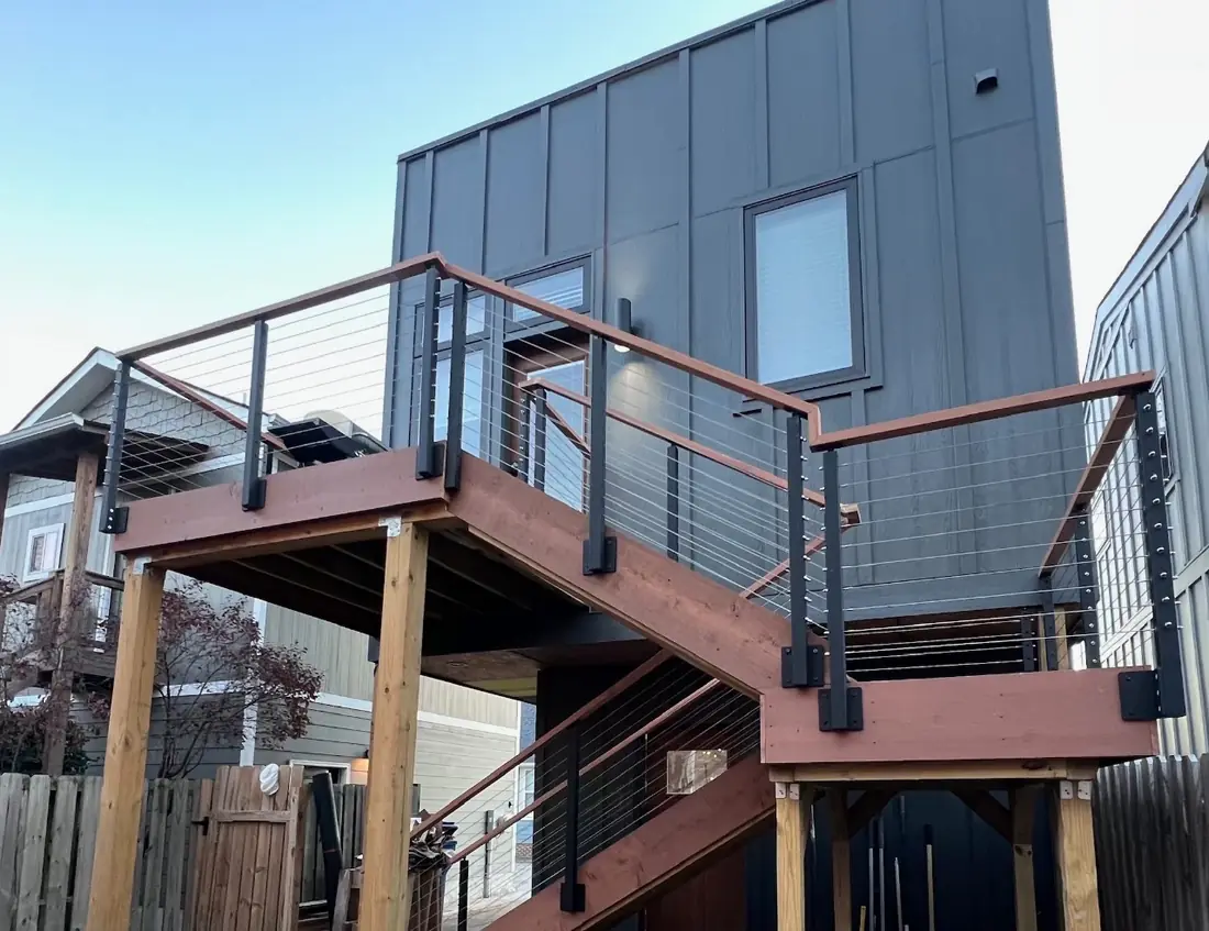 Elevated cable-rail deck and stair system on a charcoal board-and-batten home
