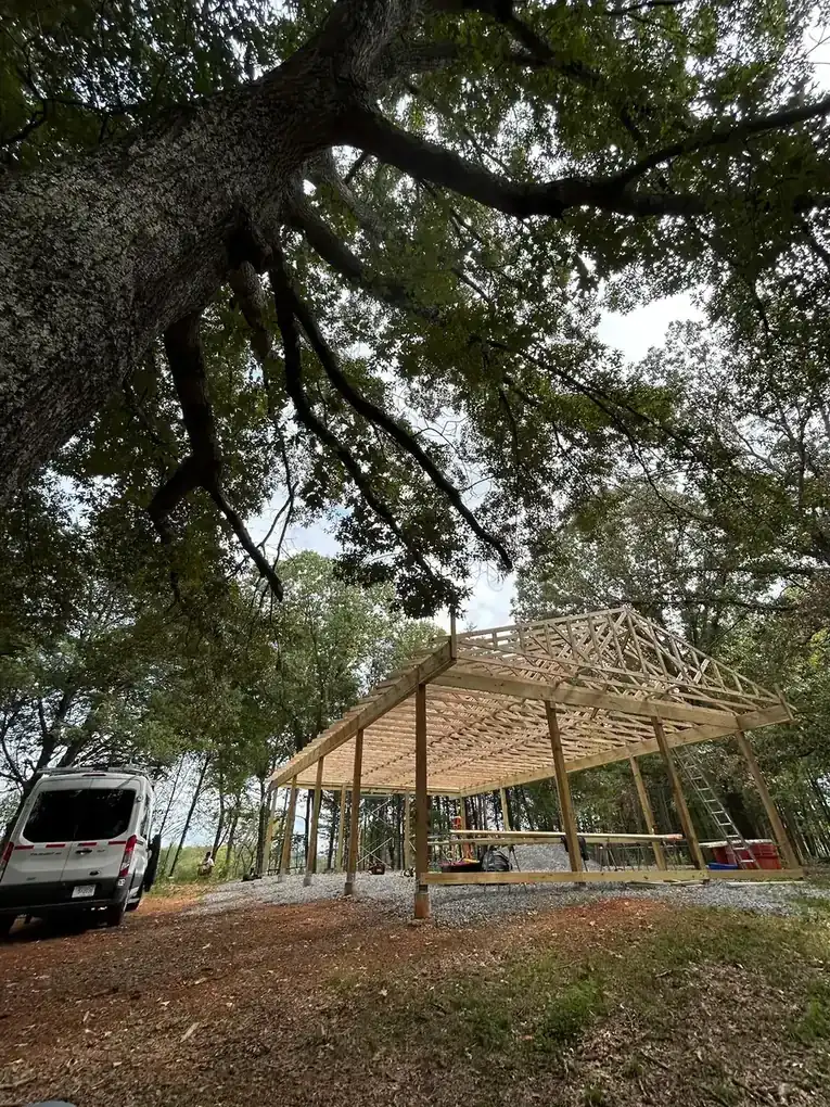 Pole barn truss frame standing under a mature oak